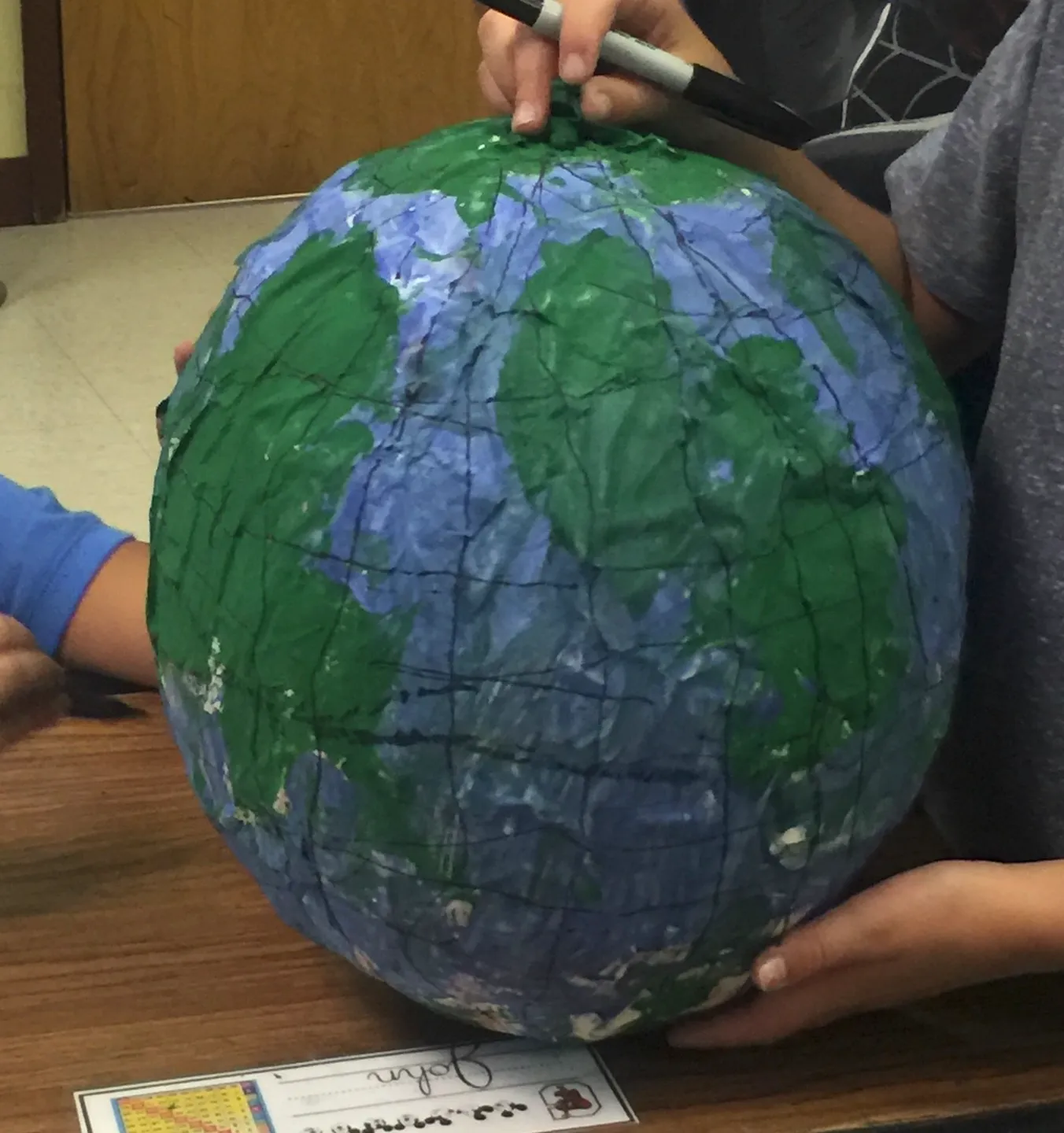 Hands holding a papier-mâché globe painted blue and green