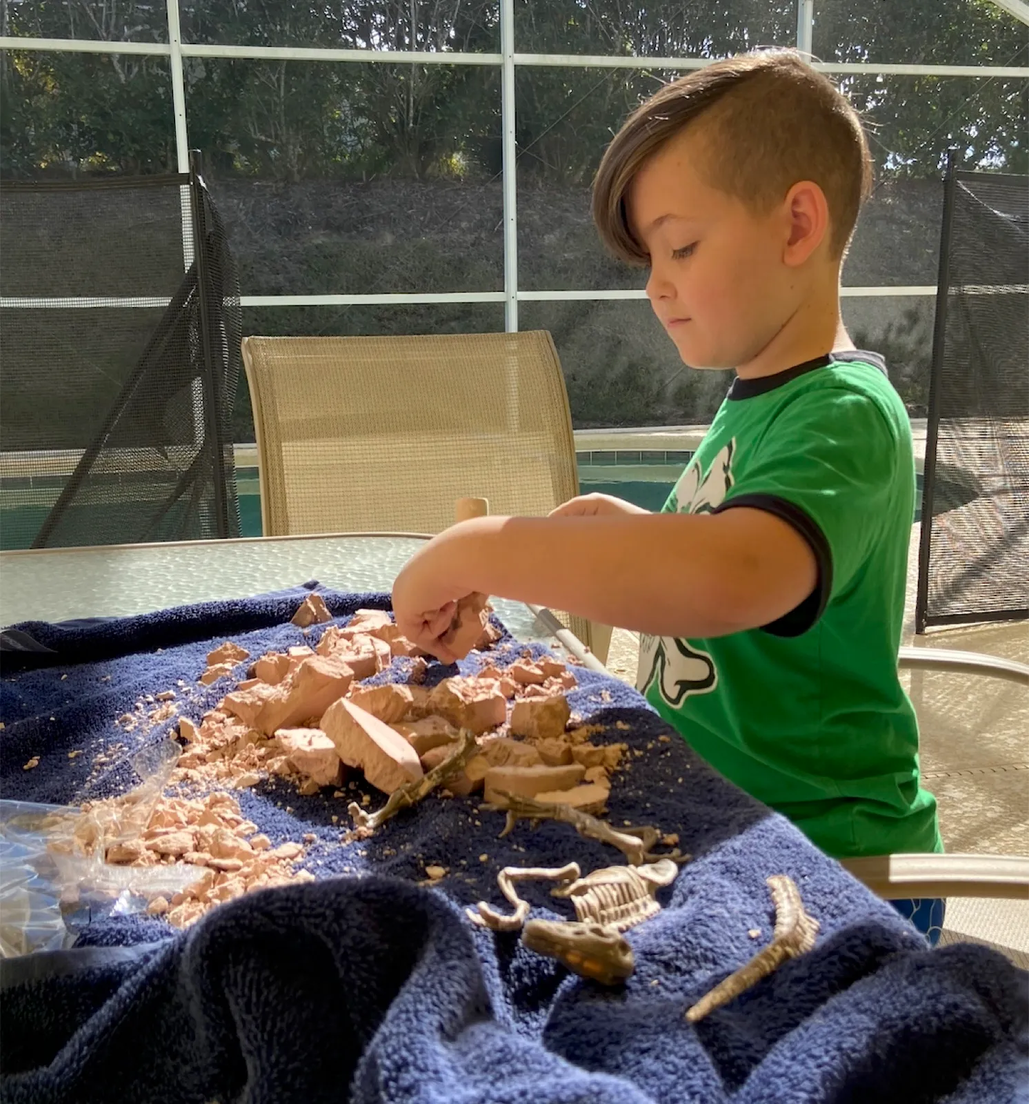 A child digging fossil bones out of clay chunks at a patio table